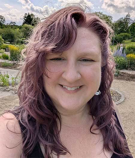 Angela, a white woman with wavy purple hair, in a garden.